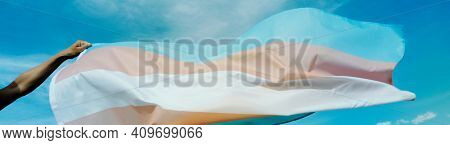 closeup of a person waving a transgender pride flag on the blue sky, in a panoramic format to use as web banner or header