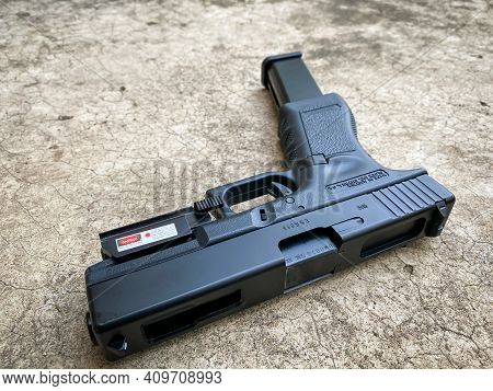 Bangkok Thailand - 21 February 2021: Air Soft Gun Glock 18C Pistol Gun With Laser Sight On The Floor