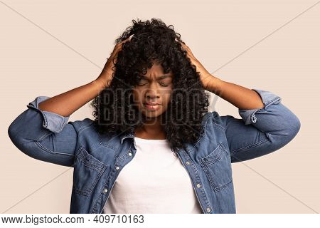 Upset Young Black Lady In Jeans Coat And White T-shirt With Curly Hair Having Headache, Touching Her
