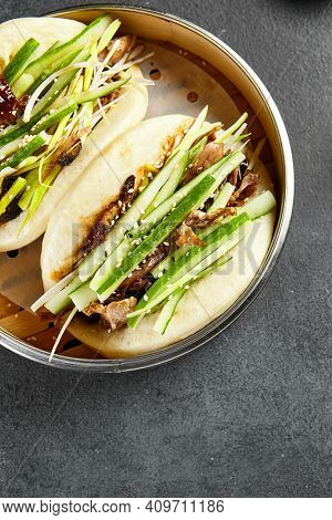 Bao bun with roast duck. Bamboo steamer on dark slate table. Chinese, asian, authentic food concept.