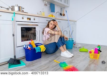 Depressed Young Housewife Feeling Tired From Domestic Chores, Sitting On Floor At Kitchen. Young Lad