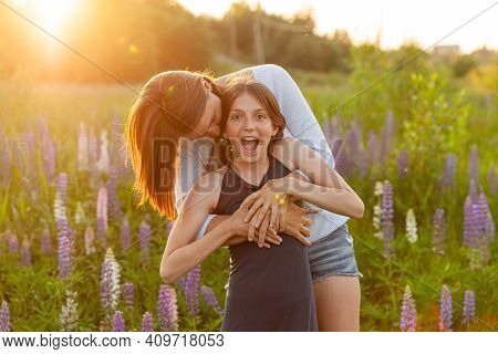Young Mother Embracing Her Child Outdoor. Woman And Teenage Girl On Summer Field With Blooming Wild