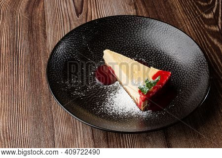 A Piece Of Cheesecake Served With Red Berry Sauce, Mint Leaf And Sugar Powder. Isolated Dish In A Bl
