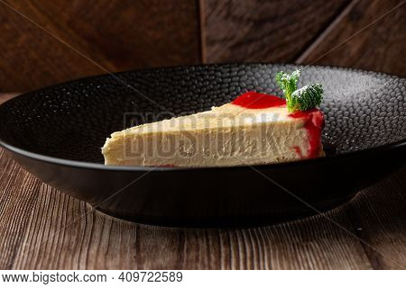 A Piece Of Cheesecake Served With Red Berry Sauce, Mint Leaf And Sugar Powder. Isolated Dish In A Bl