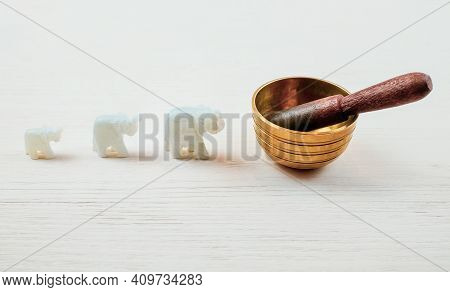 Three Elephantes Made Of Stone And Singing Bowl On White Wooden Background. Meditation And Relaxatio
