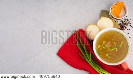 Hot Homemade Beef Bone Broth With Collagen And Amino Acids In Red Bowl With Red Napkin And Green Oni