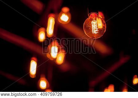 Edison Lamp On A Black Background. Incandescent Lightbulb With A Dark Background With Bokeh. Tungste