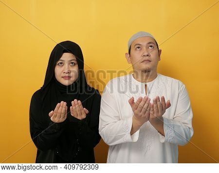 Happy Asian Muslim Couple Making Pray To God, Dua Or Do'a Gesture, Hands Raised Up, Islamic Culture,