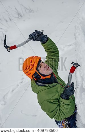 Alpinist Man With Ice Tools Axe In Orange Helmet Climbing A Large Wall Of Ice. Outdoor Sports Portra