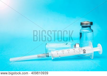 Two Ampoules Of Vaccine With A Syringe On A Blue Background.