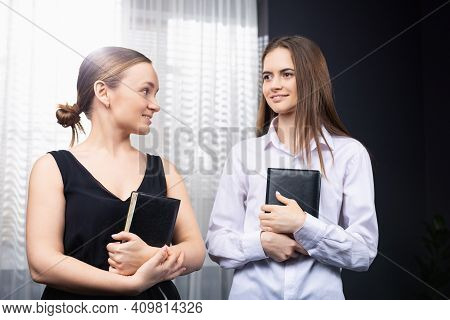 Portrait Of Two Successful Business Female Partners Sitting And Looking At Each Other With Smiles At