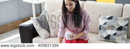 Woman Is Sitting On The Couch Holding Cup In Crayfish And With Her Other Hand Typing On Laptop Keybo