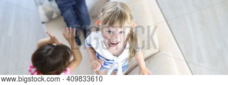 Boy And Girls Laugh And Jump On Couch At Home. Home Games For Children Concept