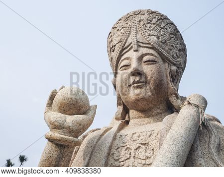 Qingdao, China - December 2017: White Carved Buddhist Sculpture Holding A Ball And Scroll At The Ent
