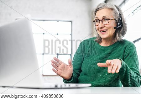 Active Mature Woman Using A Laptop For Remote Work From The Home Office. Smiling Elderly Lady Wearin