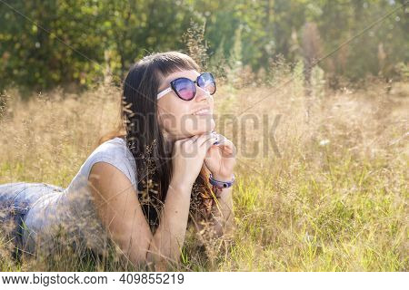 Happy Beautiful Young Woman In Sunglasses Smiles And Lies On A Meadow In The Grass In The Sunshine E