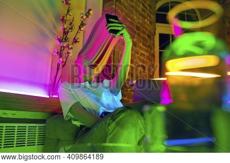 Cinematic Portrait Of Stylish Woman In Neon Lighted Interior Using A Smartphone. The Face Is Smeared