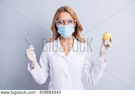 Photo Of Mature Dentis Woman In Facemask And White Coat Hold Stomatology Equipment And Apple Isolate