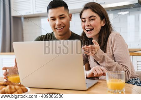 Smiling young couple onna video call via laptop computer while having breakfast