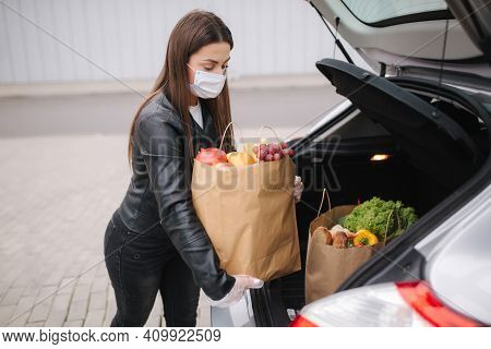 Groceries In Females Hand By The Car Truck. Woman In Protective Mask And Disposable Gloves. Fresh Fr