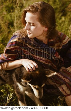 On The Steppe Grass Sits A Girl Dressed In The Style Of Hippies Or Boh And Strokes The Dog. High Qua