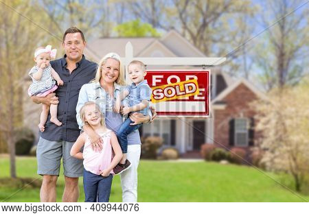 Happy Young Caucasian Family Outside In Front of Their New Home and Sold Real Estate Sign