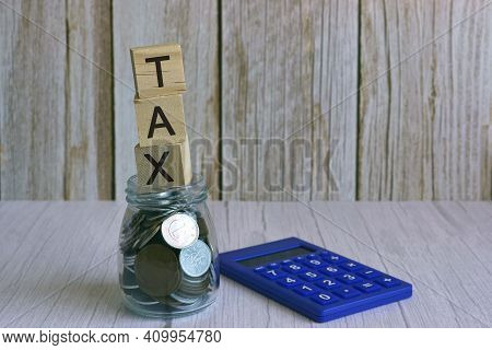 Tax Text On Wooden Block Cube On Top Of Glass Jar With Multicurrency Coins And Calculator. Tax Time 