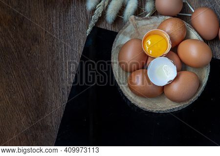Broken Chicken Egg Over Fresh Chicken Eggs (hen Eggs) Placed On Small Timber And Dried Flowers On Bl