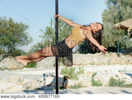 Young Pole Dancer Posing On A Portable Platform Against The Garden. Athletic Caucasian Woman Trainin