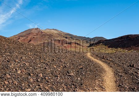 Path In Desert And Silhouette Of Volcano Del Teide Against  Blue Sky And Female Hiker With Backpack.