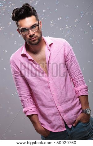 young fashion man standing emotionless with his hands in his pockets and looking at the camera while many bubbles fly around him. on a white background