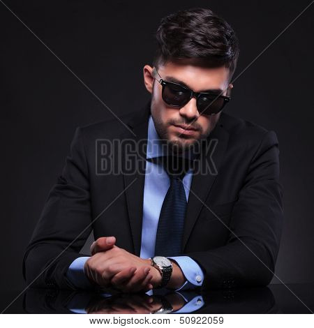 young business man holding his palms together and looking at his watch. on black background