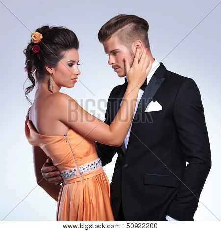 young fashion couple with woman caressing the man's face while looking at eachother. on gray background