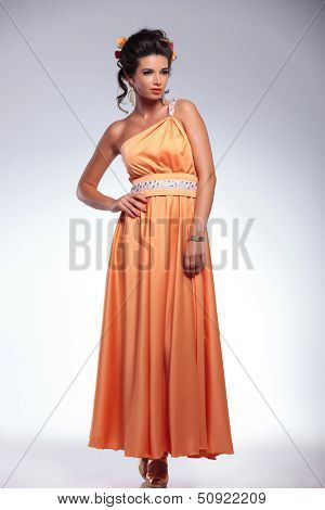 full length picture of a young fashion woman looking away while holding her hand on her hip. on gray background