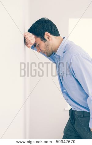 Devastated man with fist clenched leaning his head against a wall