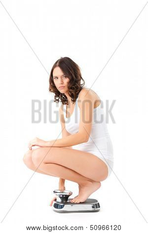 Diet and weight, young woman sitting on her haunches on a scale, she is desperate