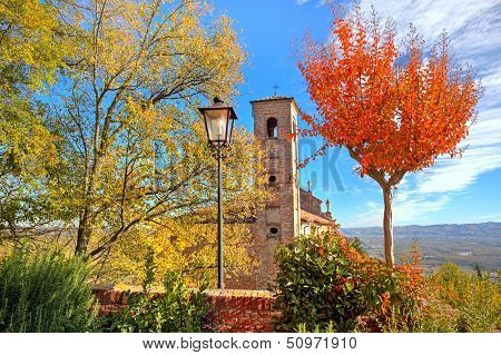 Old brick bell tower as seen among trees with red and yellow leaves in small italian town in autumn.