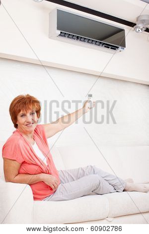 Woman holding a remote control air conditioner at home. Happy mature woman on sofa