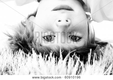 Happy little boy standing upside down on green grass in spring park, black and white