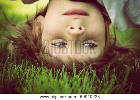 Happy little boy standing upside down on green grass in spring park, instagram effect