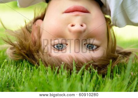 Happy little boy standing upside down on green grass in spring park
