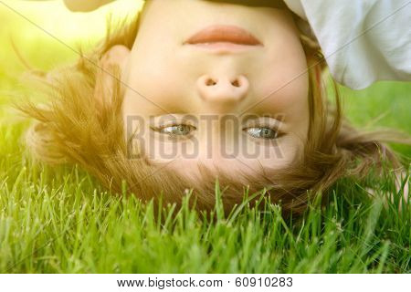Happy little boy standing upside down on green grass in spring park, toned