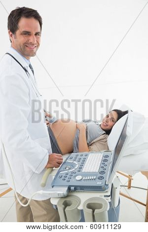 Portrait of smiling doctor performing ultrasound on expectant woman in hospital