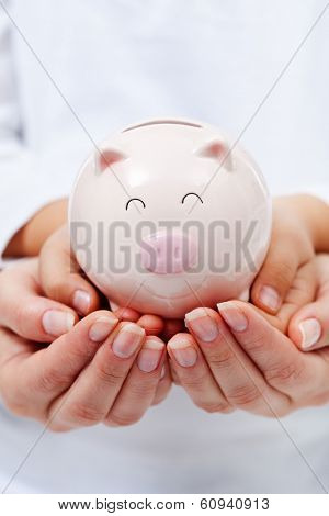 Cute small piggy bank in child hands - upheld by adult hands, financial education concept