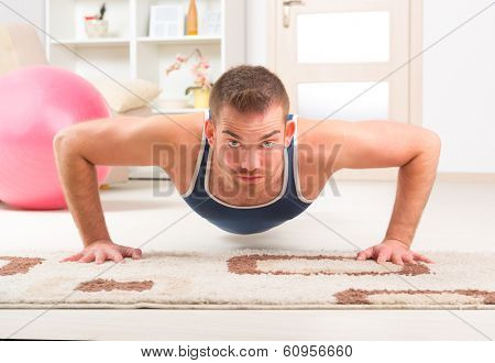 Happy attractive sporty handsome man doing push ups exercises at home