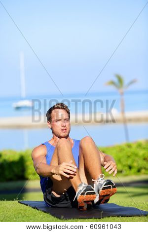 Training fitness man doing sit-ups exercise for abs outdoors. Fit male athlete cross training jackknife sit up during workout. Muscular handsome young caucasian man working out outside.
