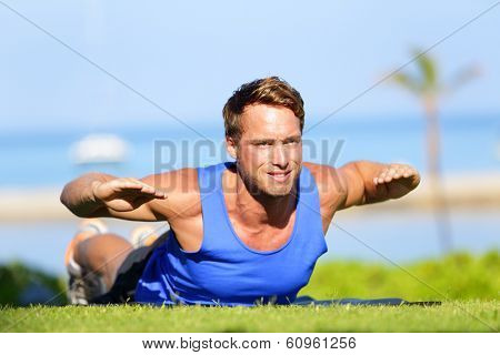 Fitness man training back extension exercise outdoor. Fit male sport athlete exercising lower back during cross training workout outside on grass in summer. Fit handsome muscular sports model.