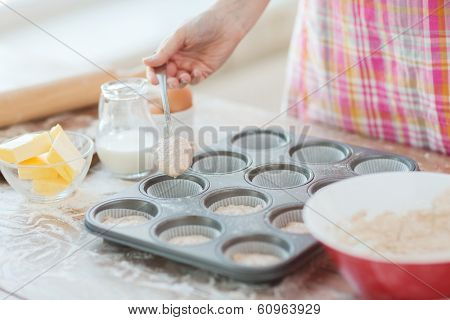 cooking and home concept - close up of hand filling muffins molds with dough