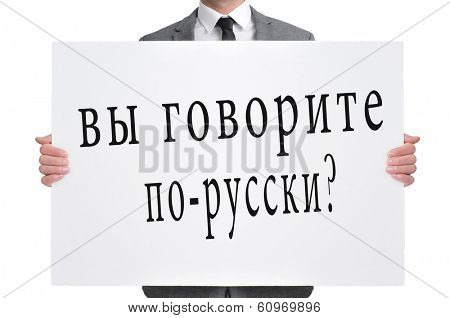 a man wearing a suit holding a signboard with the text do you speak russian? written in russian