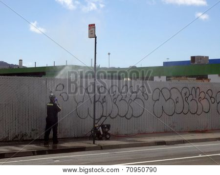 Man Uses Painting Machine To Paint Over Graffiti Tagging On Fence Along Road